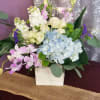 Designed in a wooden cube with hydrangea, spray roses, green buttons, purple