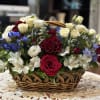 Presented in a handled basket, this colorful arrangement includes red roses, white