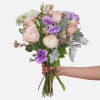 Blush ranunculus, pink roses, purple lisianthus, and wax flowers are paired with