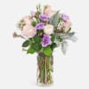 Blush ranunculus, pink roses, purple lisianthus, and wax flowers are paired with