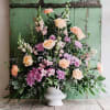 Pastel fresh flower tribute designed in a white urn. The orientation of