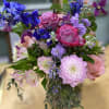 cylinder vase arranged with delphinium, roses, dahlias, alstroemeria, and stock.  