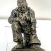 A handsomely detailed bronze finish figurine. It depicts a firefighter dressed for