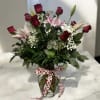Roses and pink lilies arranged in vase with greens and babies breath