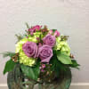 A compact modern arrangment of purple roses, mini green hydrangea and mixed