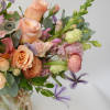 A soft pastel-colored floral arrangement, including peach roses and ranunculus, lavender clematis