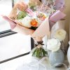 A hand-tied arrangement includes roses, hydrangeas, freesias, and ranunculus.
