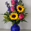 A cobalt blue vase full of bright florals. Sunflowers, , Roses, and