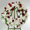 This timeless memorial wreath features red roses, fragrant white lilies, and other