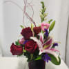 A beautiful red glass cube filled with stargazer lilies, red roses, snapdragons