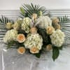 White hydrangeas, blush/peach roses, lilies, fillers and greenery in a white basket.