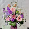 Arrangement of pink, purple and white flowers in a purple glass vase.