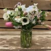 Relaxed pretty arrangement of delicate flowers in a hammered glass mason jar.