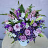 A purple and white sympathy basket featuring snapdragons, roses, lilies, and stock.