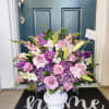 A purple and white sympathy basket featuring snapdragons, roses, lilies, and stock.