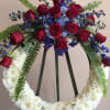 CIRCULAR WREATH WITH MUMS, HYDRANGEA, BLUE DELPHINIUM, AND RED ROSES  THE