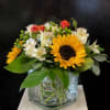 A cheerful square glass vased arrangement featuring Sunflowers, Spray Roses, Alstromeria, and