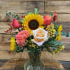 Our arrangment includes sunflowers, and peach roses in a clear vase. 
Substitutions