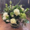 A variety of green and white flowers in a short clear vase.