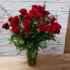 2 dozen red roses arranged in a vase filled with greenery 