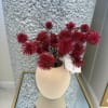 A sophisticated cream vase adorned with vibrant red pom-pom plants, adding a