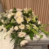 The blissful casket spray features a variety of white flowers with elegant