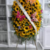 A heartfelt standing spray filled with bright sunflowers and adorned with colorful
