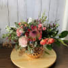 This arrangement features red/pink/orange themed flowers with a rose gold vase giving
