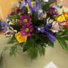 Iris, yellow roses, purple daisys, and alstromeria arraned in a glass vase