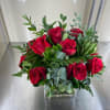Red roses with mixed greens in a glass vase.