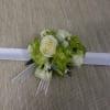 A corsage consisting of white spray roses with a touch of green.