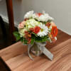 A peach colored vase filled with whites, peaches and orange colored blooms