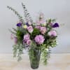 Purple and lavender roses and lisianthus are arranged in a tall vase