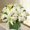 A beautiful arrangement of white lilies and roses in a square vase.