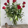 A dozen roses with mixed green filler in a tall glass vase.