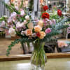 Roses, ranunculus, spray roses, lisianthus, snapdragons and eucalyptus in a tall clear