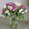White and purple roses are arranged with purple waxflowers and greenery to