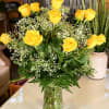 A dozen yellow roses vased with filler. 