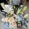 A bouquet composed of white roses, white lilies, blue hydrangeas, and lush