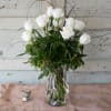 One dozen long stem white roses beautifully arranged in a bed of