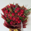 A bold hand-tied bouquet featuring red roses, burgundy blooms, and tropical greens