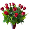 Dozen red roses mixed with greens in a tall red glass vase.