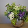 A textured arrangement in a spherical mercury vase with kale and other