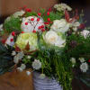 A holiday arrangement that includes a combo of green textures, red flowers
