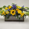 A wooden box filled with blue and yellow flowers including roses, sunflowers