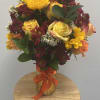 This vibrant arrangement features golden sunflowers, yellow and peach roses, burgundy mums