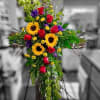 A beautiful cross-shaped standing spray featuring vibrant sunflowers, classic red roses, and