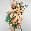 Delicately adorned with an array of peach blooms, including roses, gerberas, and