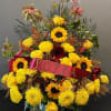 A bright one sided arrangement with yellow roses, sunflowers and filler flowers.