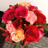 Fresh floral arrangement with roses and lilies in red art glass vase.